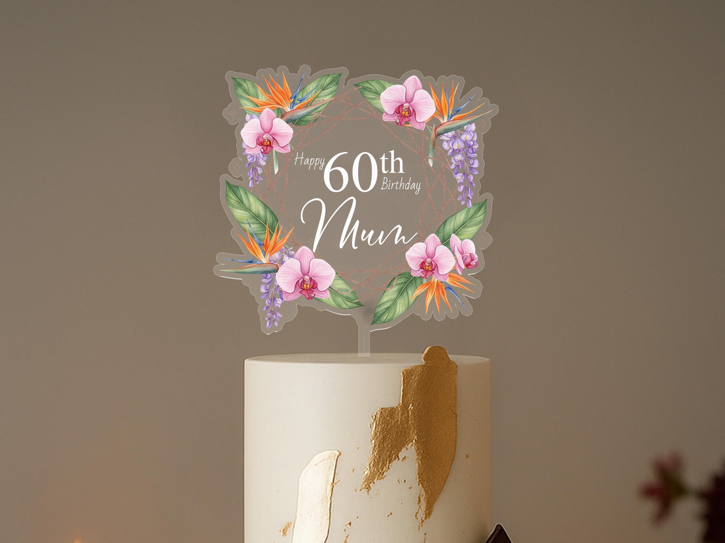 A white cake with a floral topper that says "Happy 60th Birthday Mum" on it.