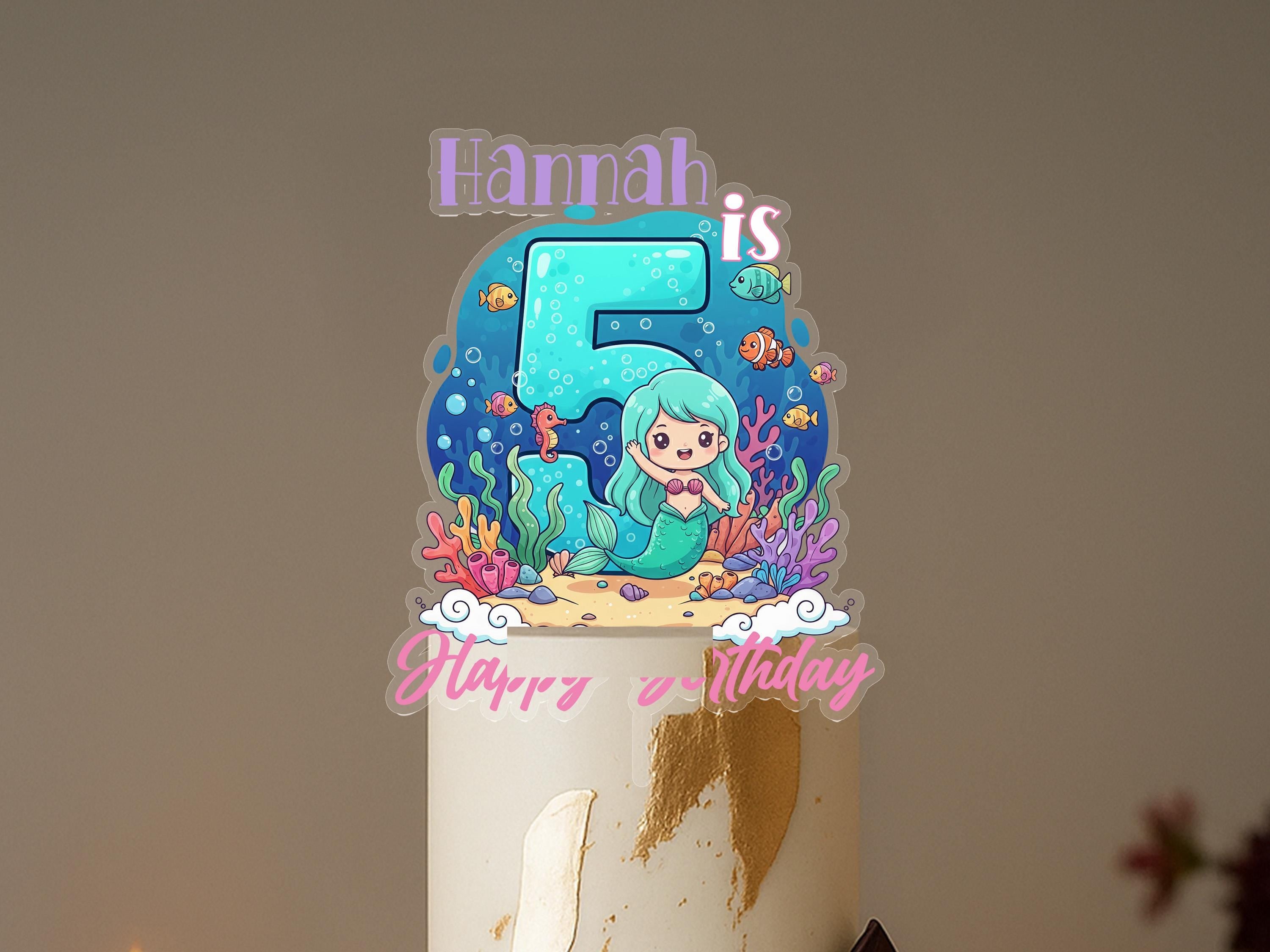 A birthday cake with a mermaid-themed topper, featuring the name "Hannah" and the number 5.