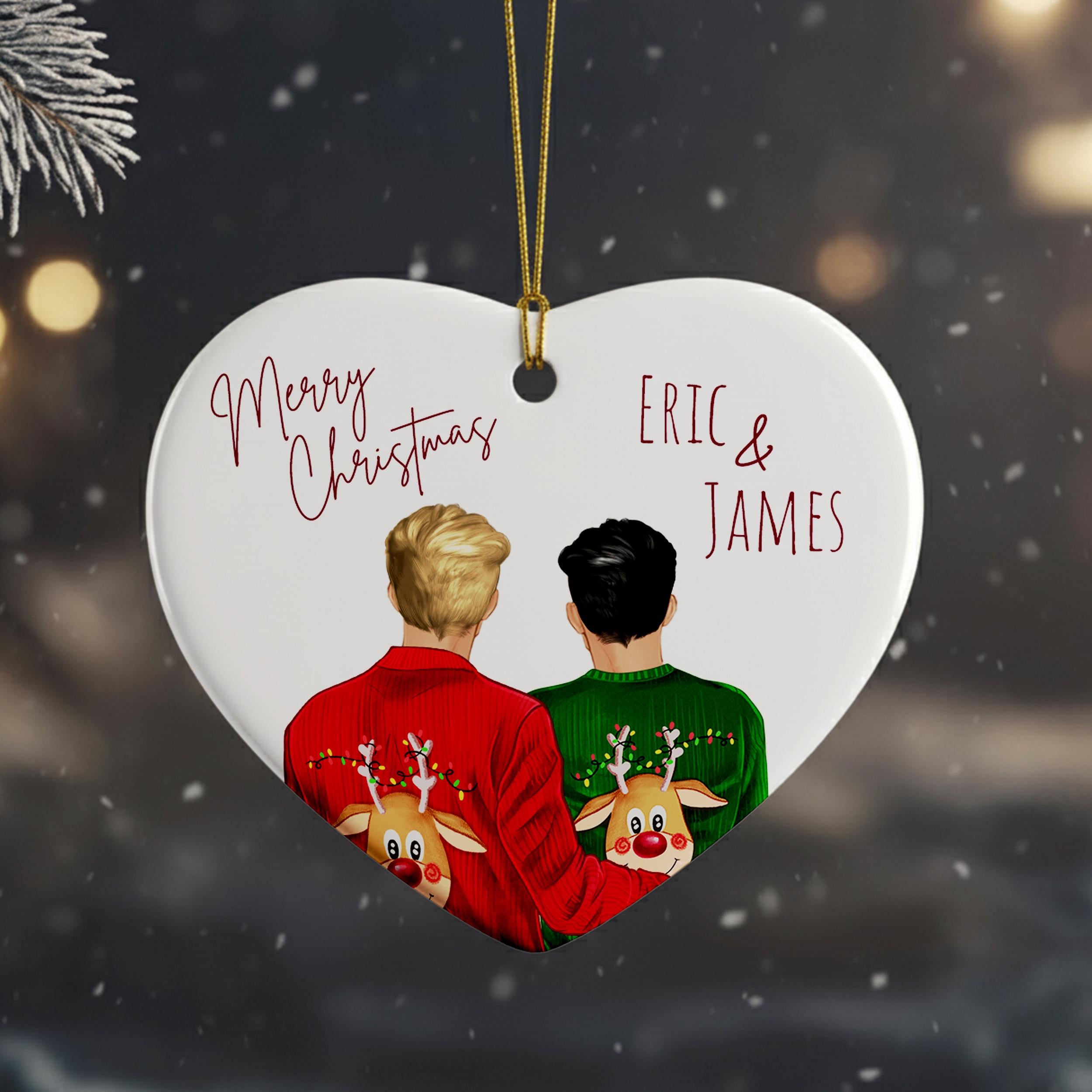 A heart-shaped ornament with two people wearing Christmas sweaters, one red and one green, with reindeer on their backs. The ornament has a string attached to it.