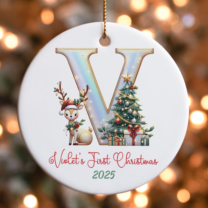 A white ornament with a large letter &quot;V&quot; and a small deer, along with a Christmas tree and presents, is hanging against a background of blurred lights.