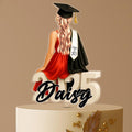 Personalised graduation cake topper featuring a female graduate in a red dress with long blonde hair, sitting on "2025" and holding a diploma, custom name Daisy in script.