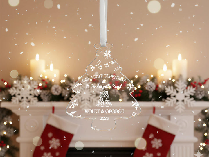 A clear Christmas ornament hangs in front of a fireplace, with a snowy background and lit candles.