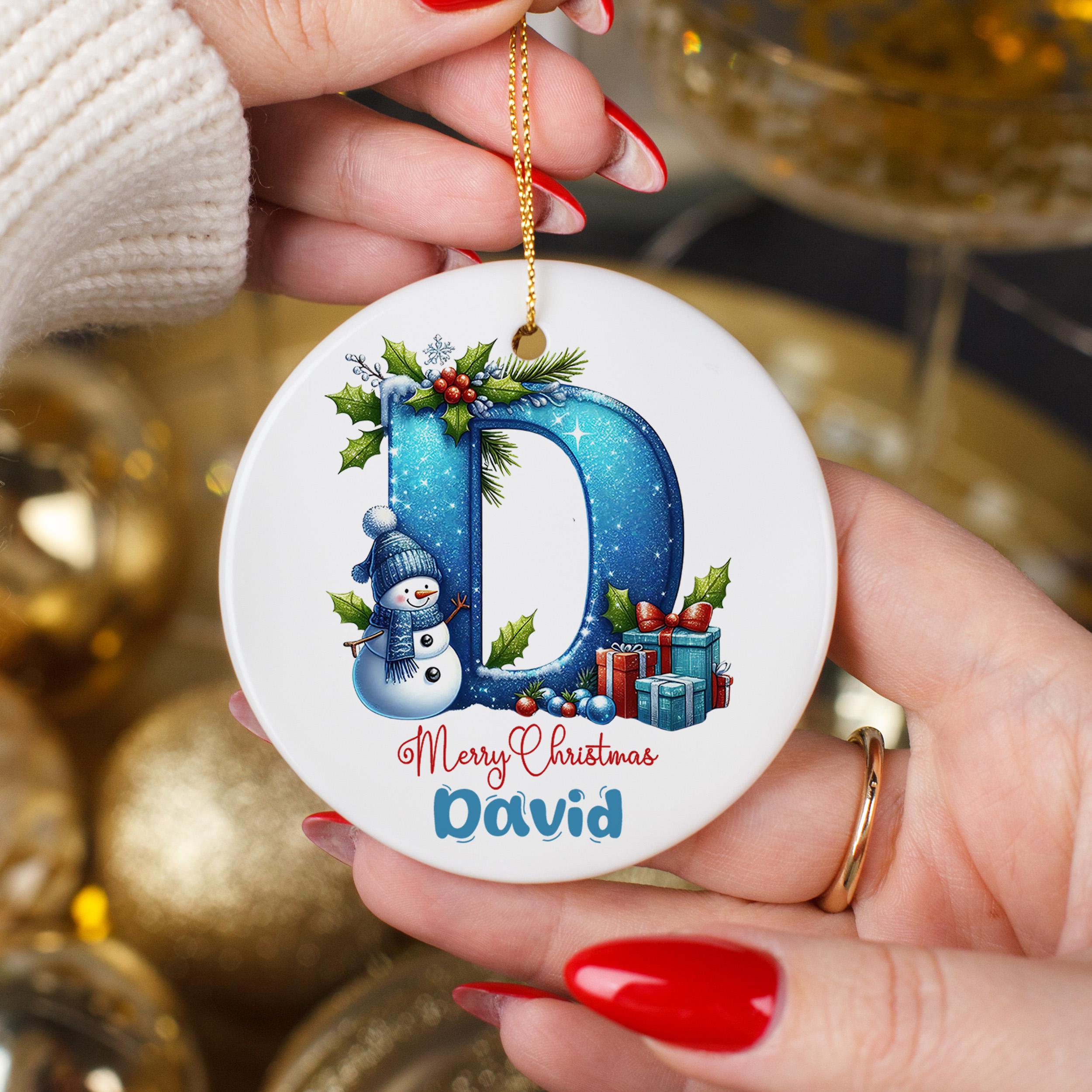 A person's hands holding a round ornament with a snowman and presents, with a personalized message on it.