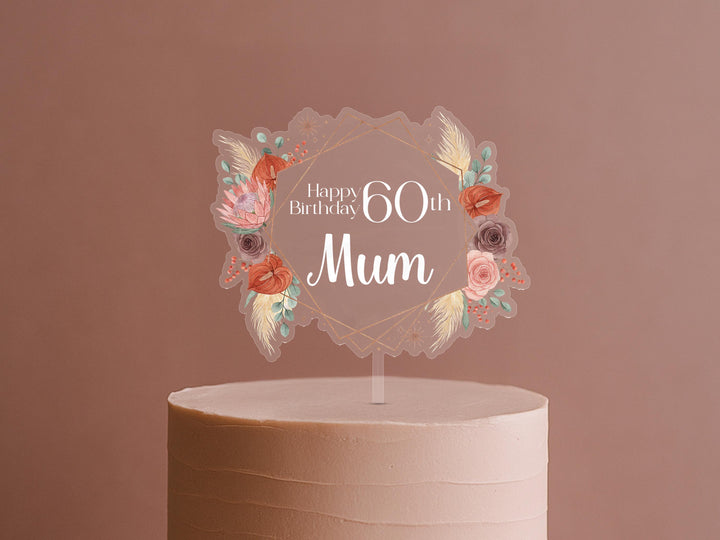 A cake topper with a floral design and the text &quot;Happy Birthday 60th Mom&quot; on it.