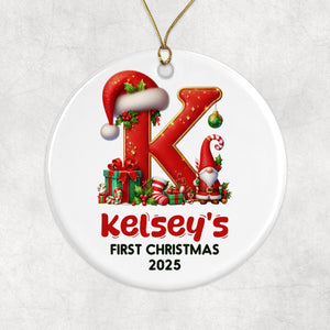 A white oval ornament with a red letter "K" and various Christmas-themed elements, including a Santa hat, presents, and a gnome. The ornament is labeled "Kelsey's First Christmas 2020".