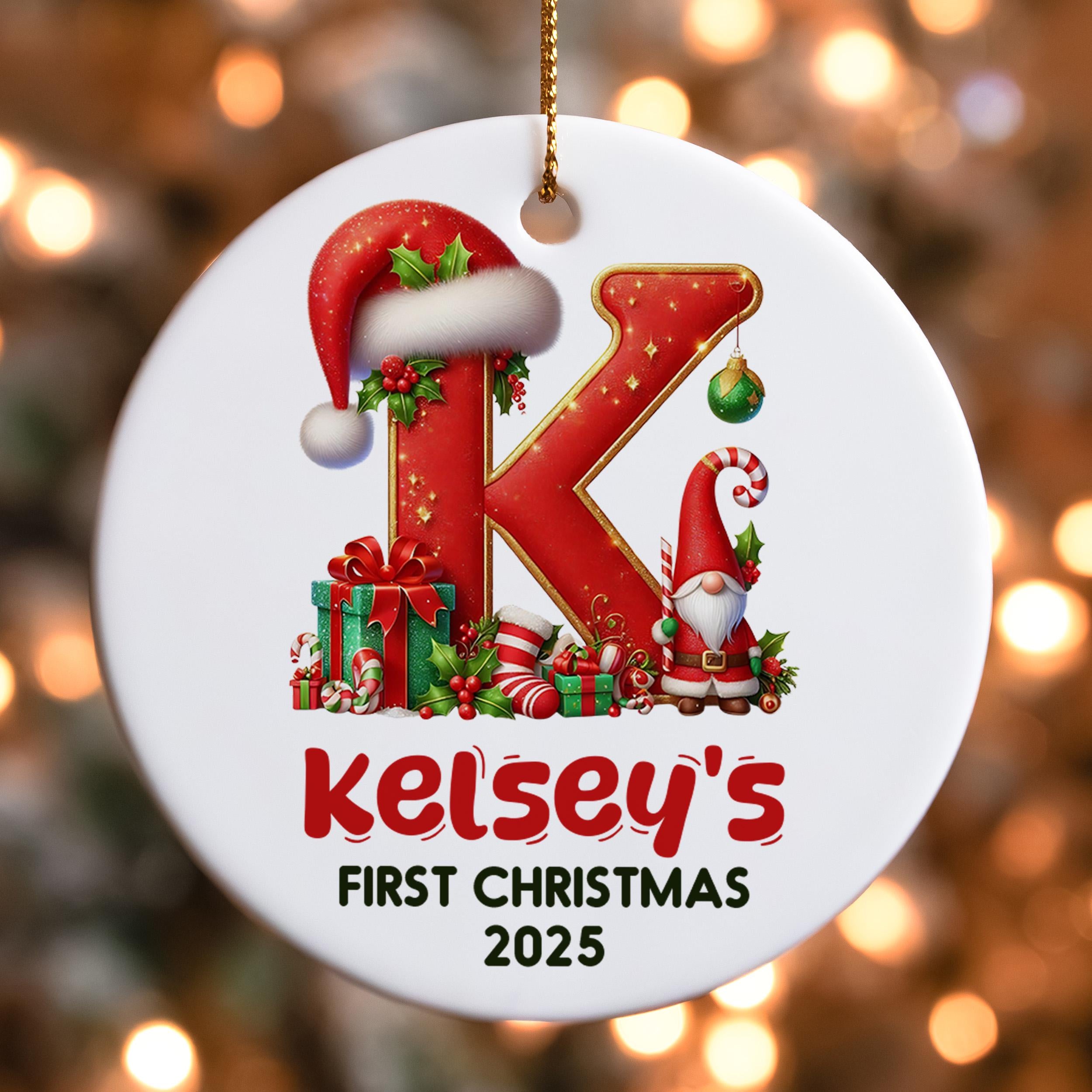A white ornament with a red letter "K" and various Christmas-themed decorations, including a Santa hat, presents, and a gnome. The ornament is labeled "Kelsey's First Christmas 2015".