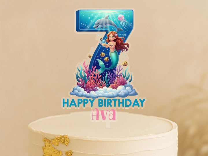 A birthday cake topper featuring a mermaid character and underwater elements, with the text &quot;Happy Birthday Ava&quot; below.