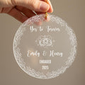 Personalised engagement Christmas ornament held in hand showing frosted acrylic design with Yes to Forever text, wedding rings with hearts and sparkles, couple names Emily and Henry, Engaged 2025, surrounded by holly leaf and berry border with gold ribbonRetry