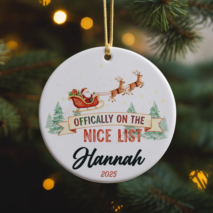A white ornament with a Santa Claus sleigh and reindeer, along with the text &quot; Officially on the NICE LIST Hannah 2020&quot;.