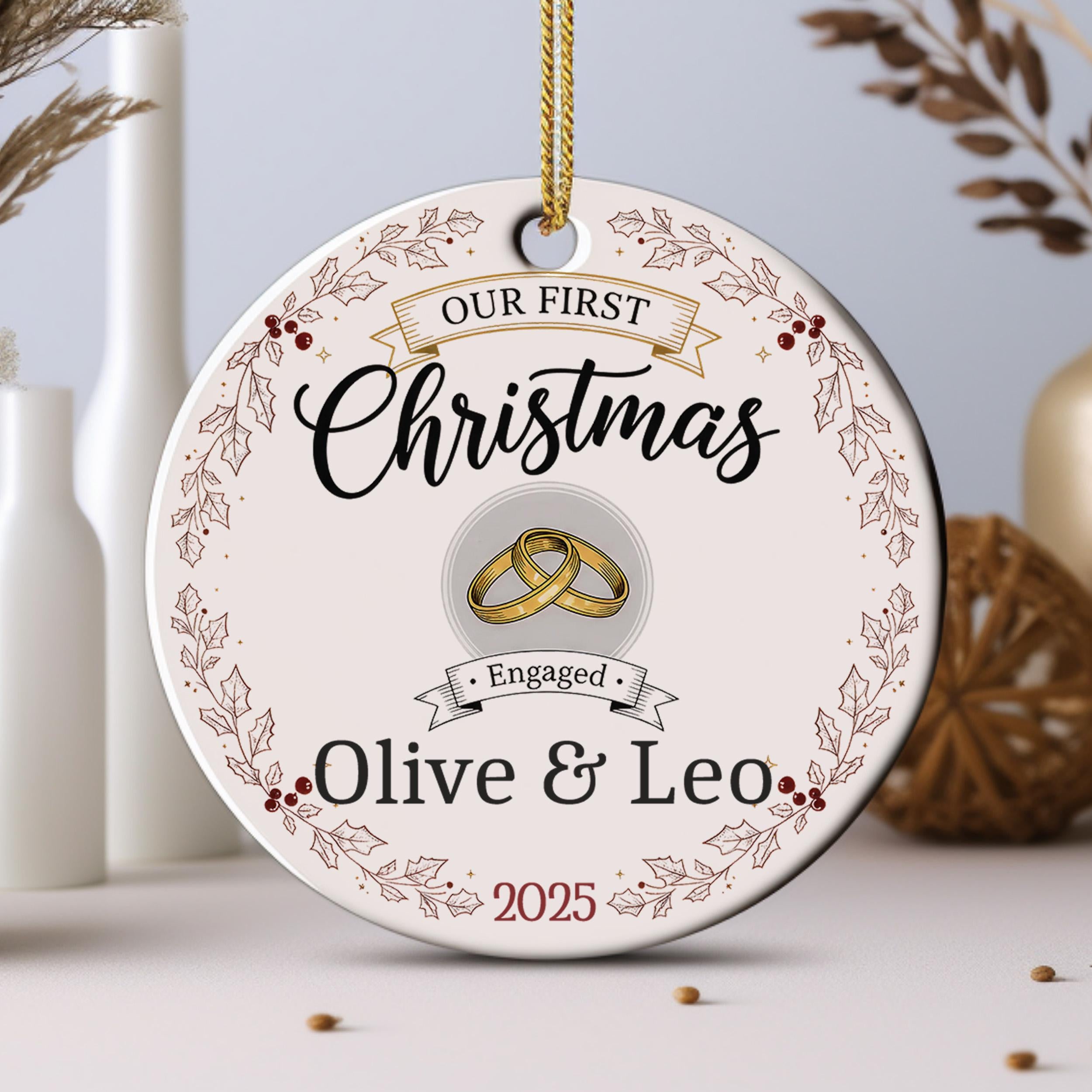 A Christmas ornament with the text "Our first Christmas" and "Engaged Olive & Leo" along with a graphic of a couple's wedding rings.