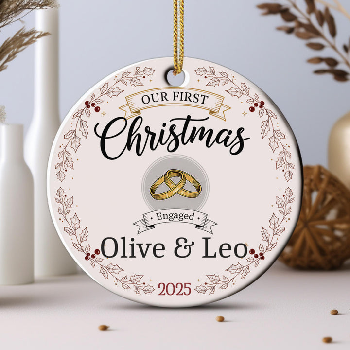 A Christmas ornament with the text &quot;Our first Christmas&quot; and &quot;Engaged Olive & Leo&quot; along with a graphic of a couple&#39;s wedding rings.