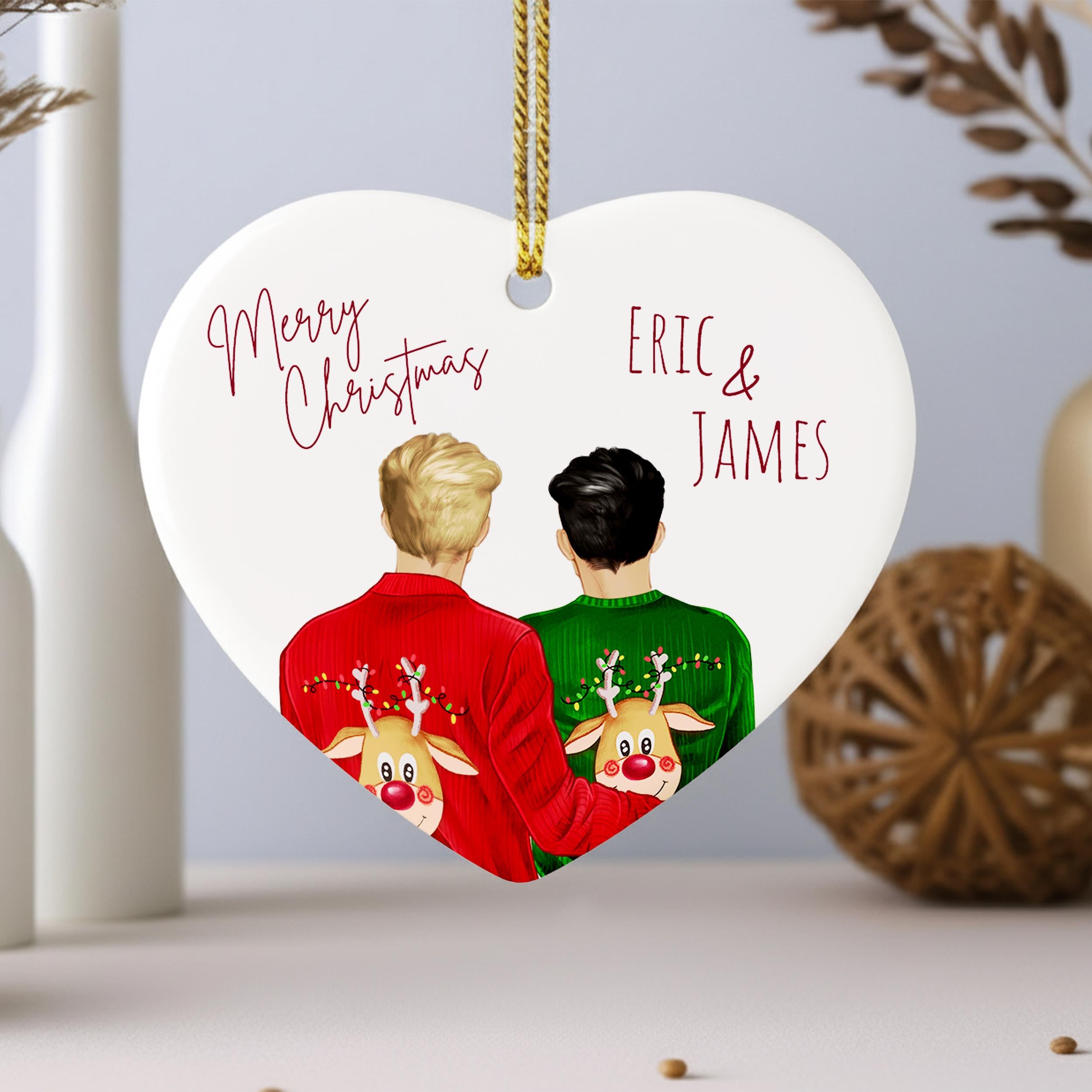 A heart-shaped ornament with two people wearing Christmas sweaters, one in red and one in green, with the text "Merry Christmas Eric & James" written above them.