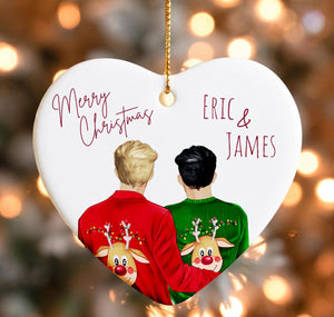 A heart-shaped ornament with two people wearing Christmas sweaters with reindeer designs. The ornament has a "Merry Christmas" message and the names "ERIC & JAMES" written on it.