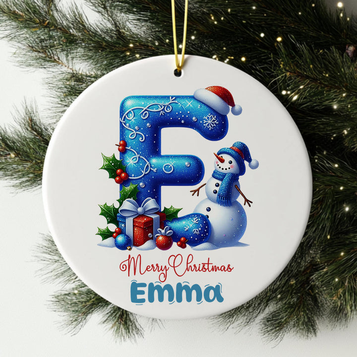 A white Christmas ornament with a snowman and presents, featuring the letter &quot;F&quot; and the text &quot;Merry Christmas Emma&quot;.
