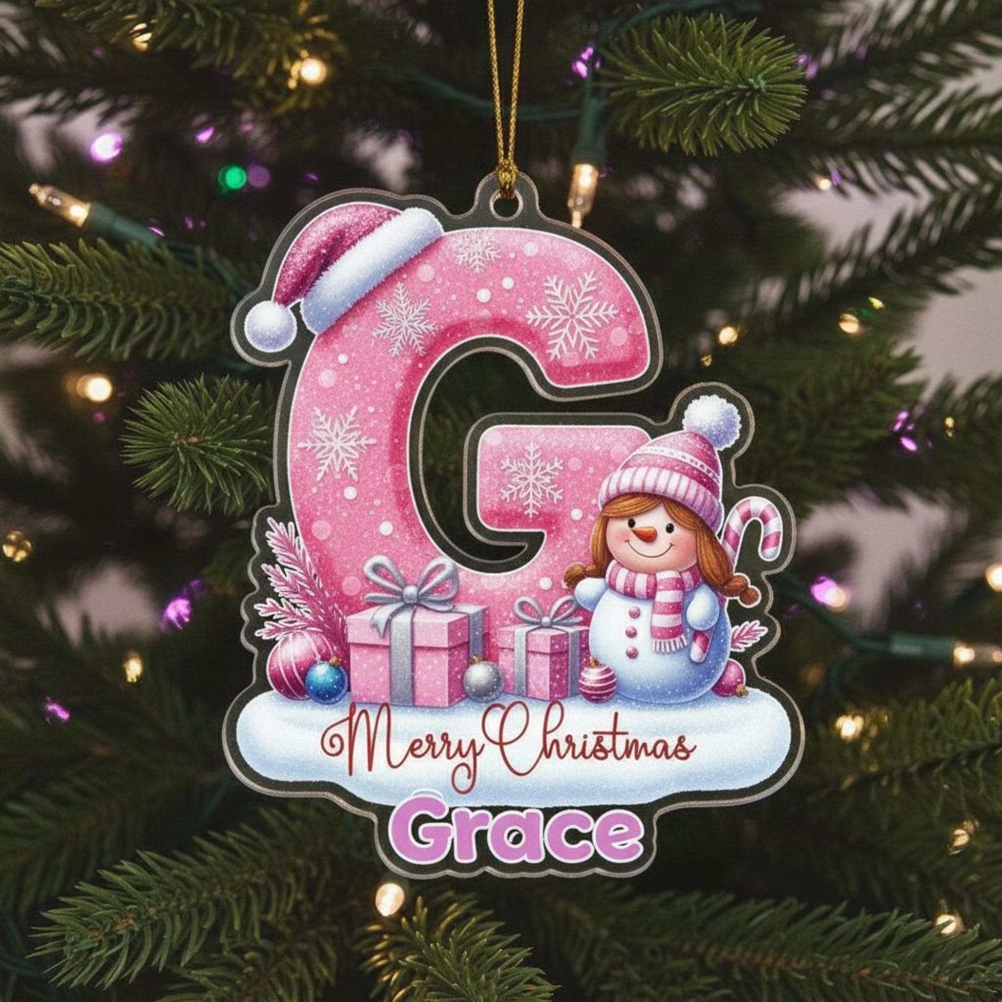 A pink snowflake ornament with a cartoon snowman and presents, hanging on a Christmas tree.