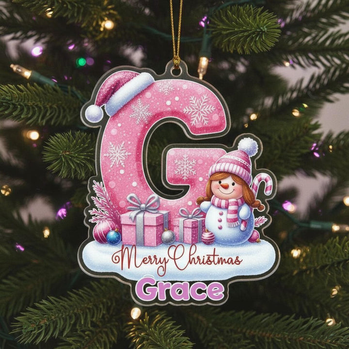 A pink snowflake ornament with a cartoon snowman and presents, hanging on a Christmas tree.