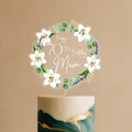 Personalised acrylic cake topper featuring elegant circular wreath of white lilies, eucalyptus leaves, lavender sprigs with Happy 70th Birthday Mum text on green and gold celebration cake