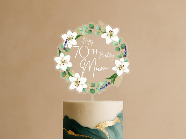 Personalised acrylic cake topper featuring elegant circular wreath of white lilies, eucalyptus leaves, lavender sprigs with Happy 70th Birthday Mum text on green and gold celebration cake