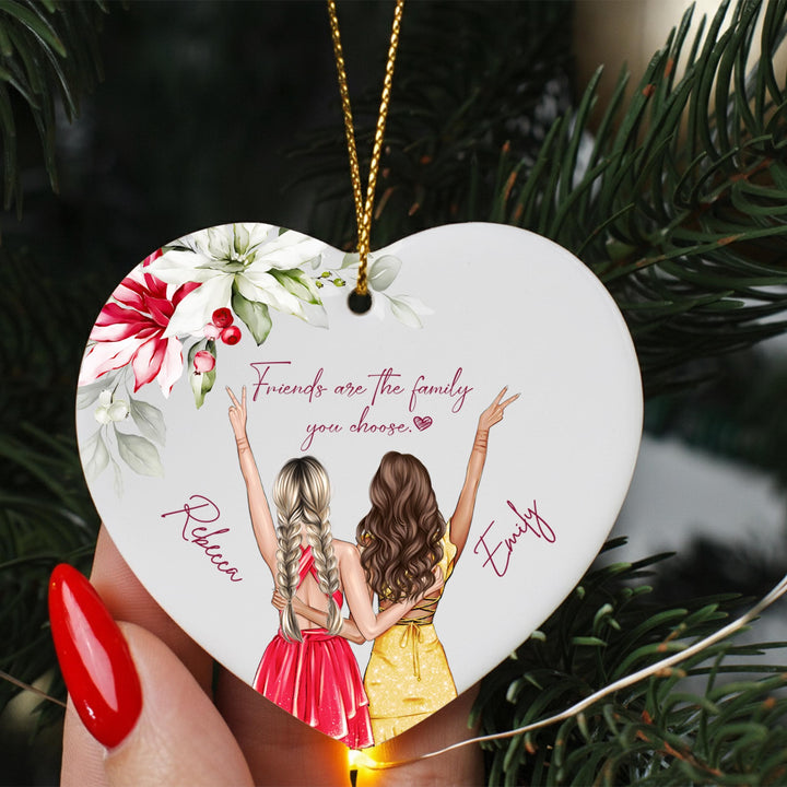 A heart-shaped ornament with two women in a loving embrace, surrounded by flowers and the text &quot;Friends are the family you choose&quot;.