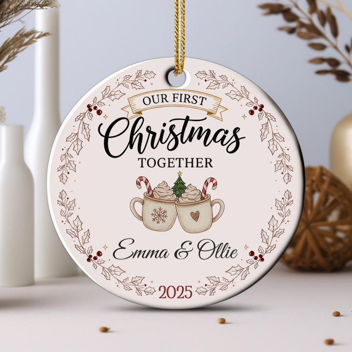 A Christmas ornament with the text &quot;Our first Christmas together&quot; and an illustration of two mugs with hot chocolate and candy canes.