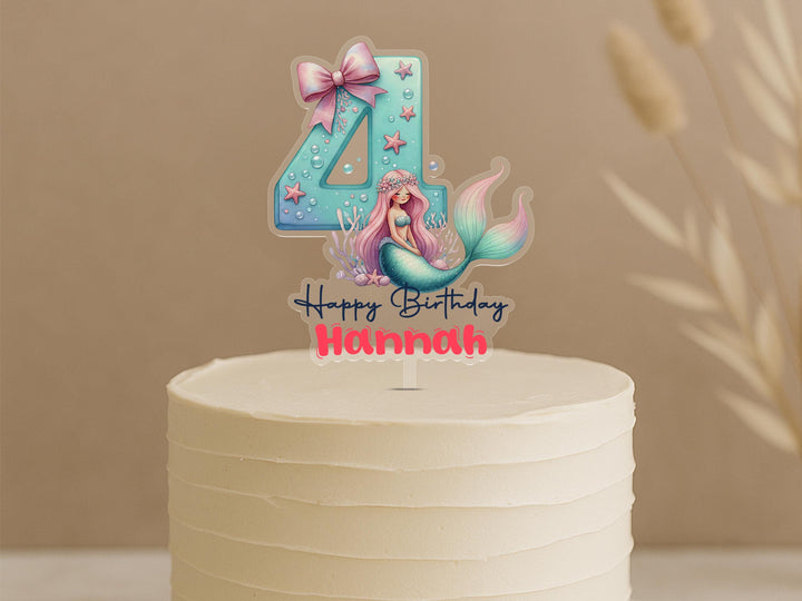 Personalised mermaid birthday cake topper featuring aqua number 4 with pink bow, starfish, bubbles, beautiful mermaid with pink hair and custom name Hannah on white celebration cake