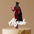 Personalised Muslim graduation cake topper featuring a hijabi female graduate in a red dress and cap, with custom name, displayed on elegant gold-accented cake.
