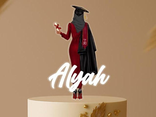 Personalised Muslim graduation cake topper featuring a hijabi female graduate in a red dress and cap, with custom name, displayed on elegant gold-accented cake.