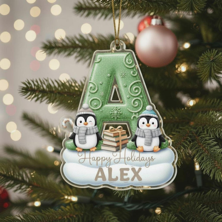A green ornament shaped like the letter &quot;A&quot; with two penguins sitting on a snowy surface, surrounded by Christmas lights and ornaments.