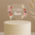 Personalised 60th birthday cake topper featuring boho diamond frame with coral roses, pink flowers, pampas grass and custom name Mum on white celebration cake