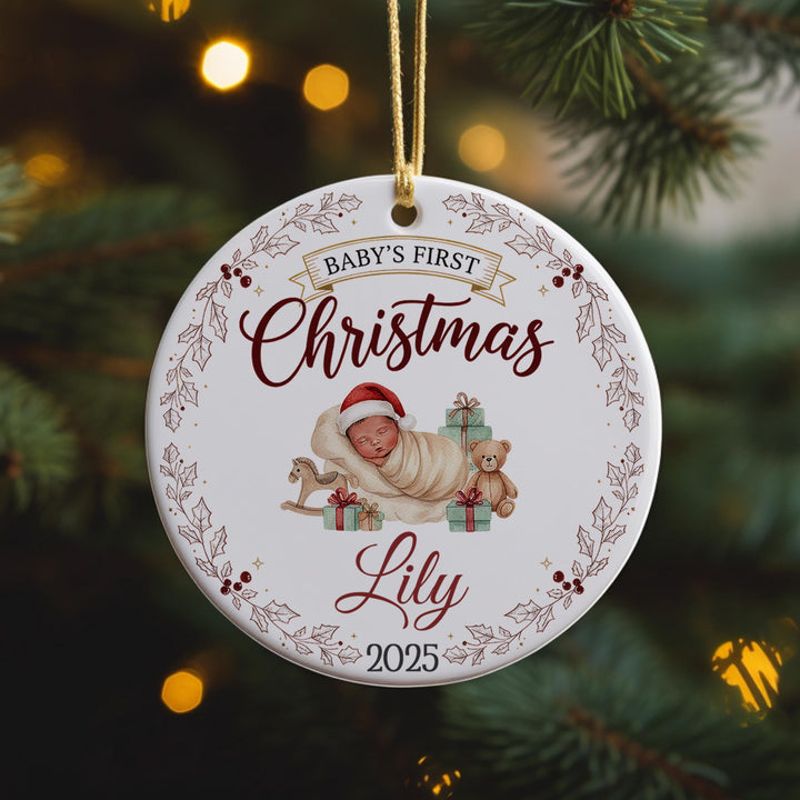 A white ornament with a baby and a teddy bear, surrounded by a decorative border, hangs on a Christmas tree.