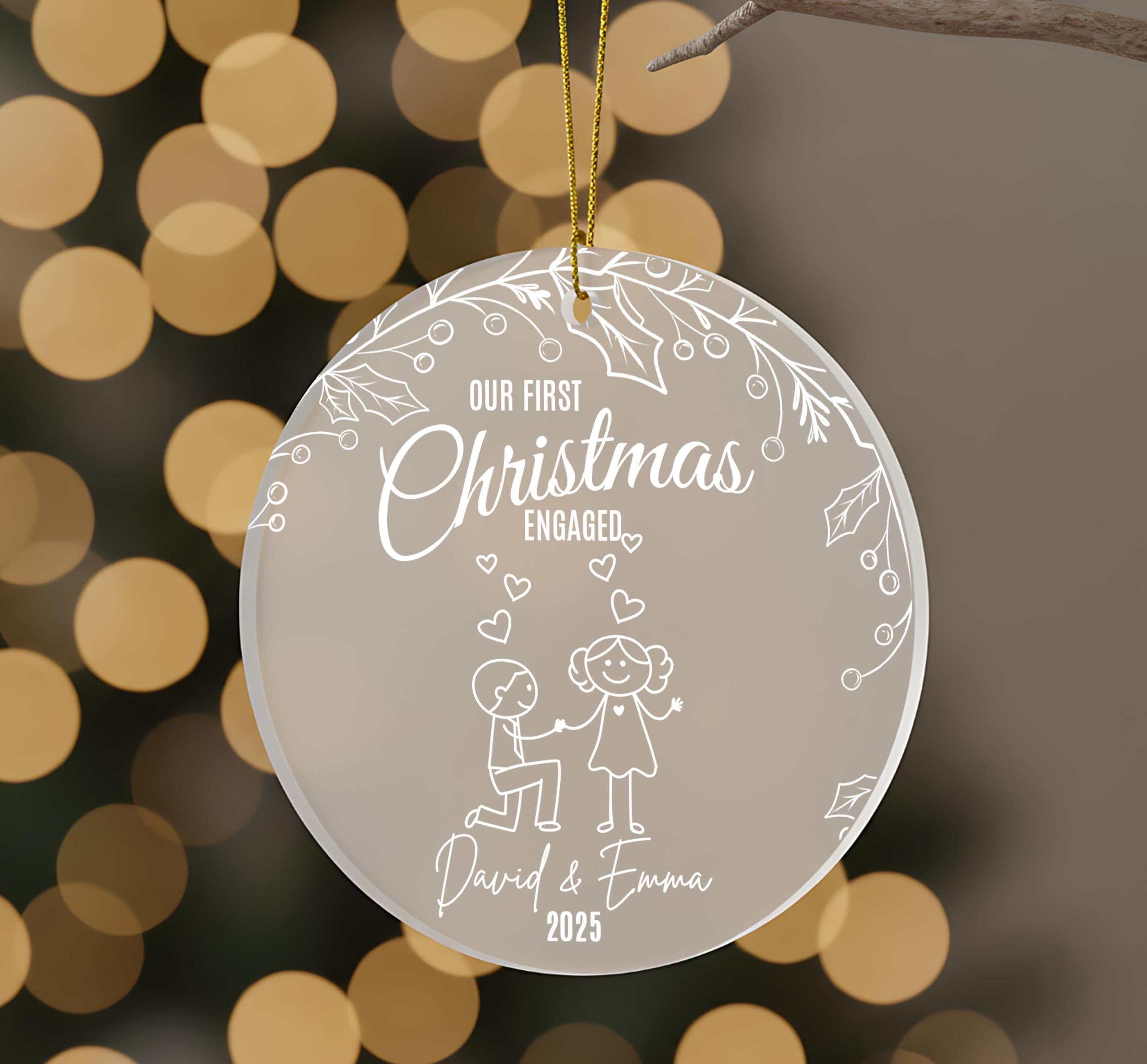 A Christmas ornament with a couple of people, one kneeling and the other standing, surrounded by hearts and leaves. The text on the ornament reads "Our first Christmas engaged David & Emma 25".