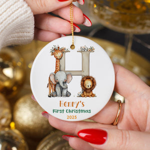 A person's hands holding a white ornament with a letter "H" and illustrations of a giraffe, elephant, and lion.