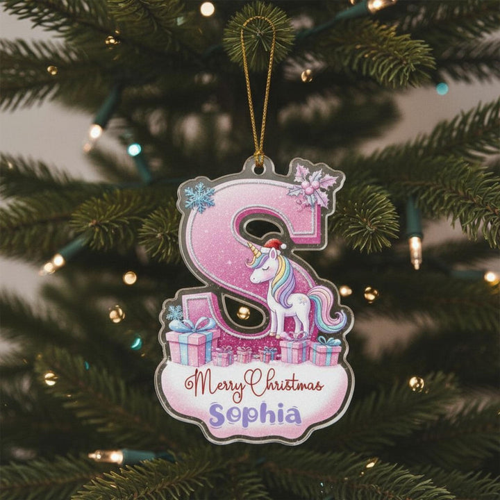 A pink ornament with a unicorn and presents is hanging on a Christmas tree.