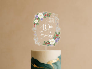 A birthday cake with a clear topper that says "Happy Birthday Emily" surrounded by a floral design.