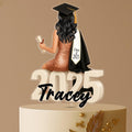Personalised graduation cake topper featuring a female graduate in a red dress with long hair, black cap and gown, sitting on large “2025” numbers, and a custom name, displayed on a celebration cake.