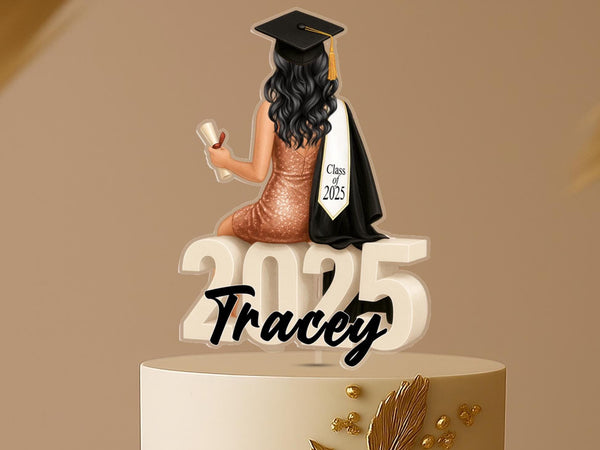 Personalised graduation cake topper featuring a female graduate in a red dress with long hair, black cap and gown, sitting on large “2025” numbers, and a custom name, displayed on a celebration cake.