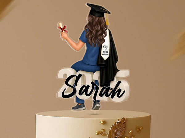 Personalised nurse graduation cake topper with a female graduate in scrubs and gown, sitting on “2025,” for Class of 2025, custom acrylic decoration.