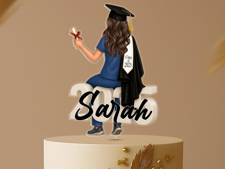 Personalised nurse graduation cake topper with a female graduate in scrubs and gown, sitting on “2025,” for Class of 2025, custom acrylic decoration.