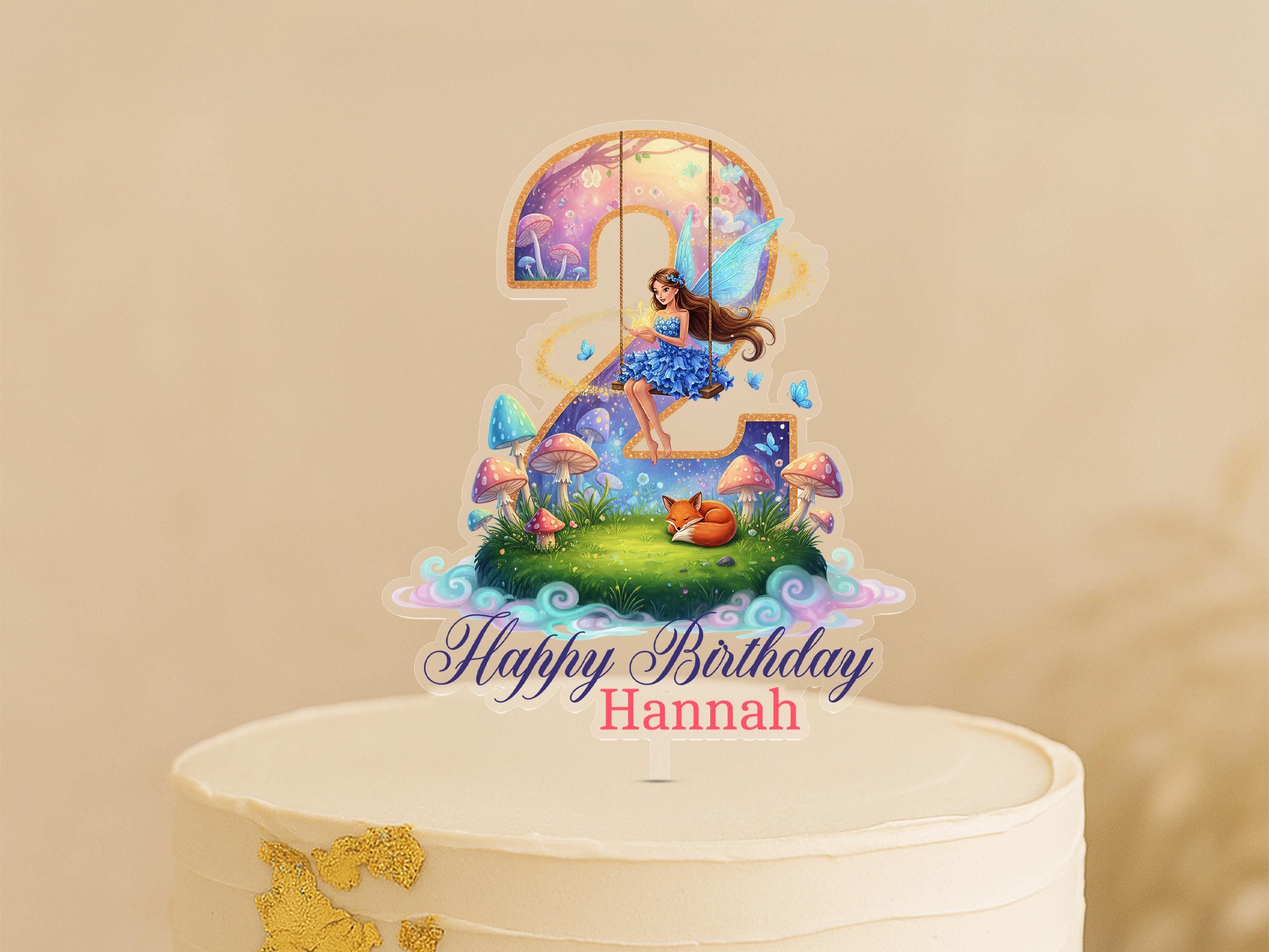 A birthday cake topper with a fairy and a number 2, along with the text "Happy Birthday Hannah".