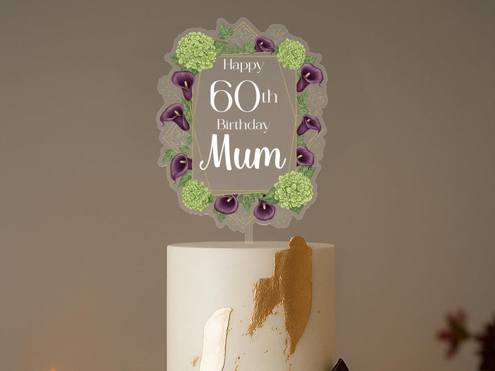 A white cake with a decorative topper that says &quot;Happy 60th Birthday Mum&quot; surrounded by purple flowers.