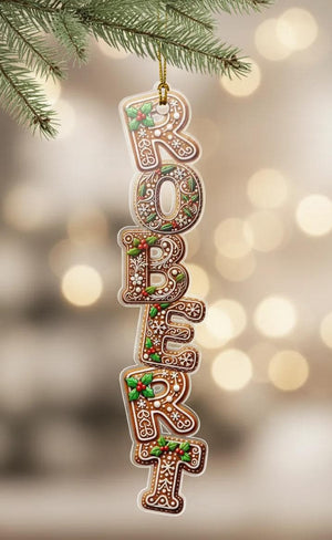 A decorative ornament made of gingerbread letters spelling out the name "Robert" hanging from a branch of a pine tree.