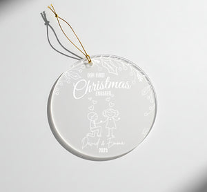 A clear glass ornament with a gold string attached, featuring a design of a couple and the text "Our first Christmas engaged David & Emma 2015".