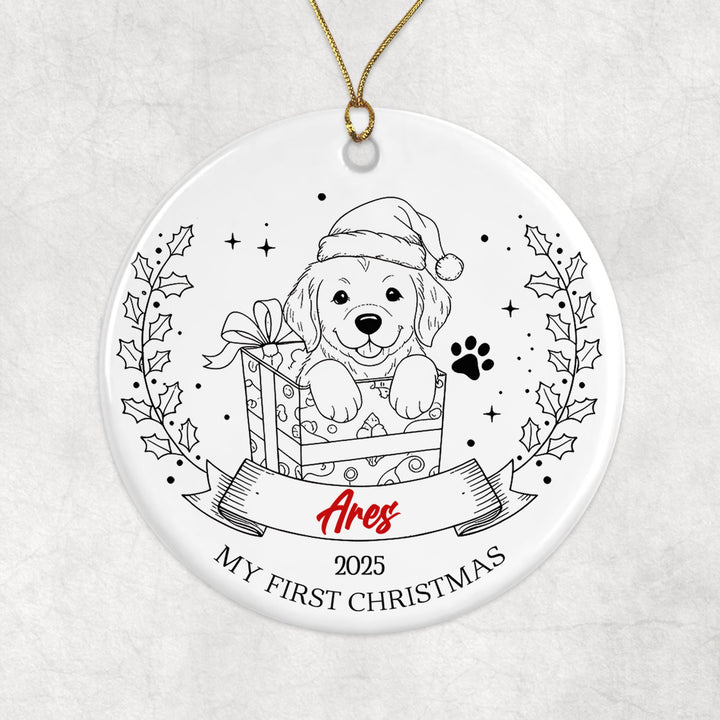 A white ornament with a black and white illustration of a dog wearing a Santa hat, holding a gift box, and surrounded by holly leaves and stars.