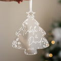 A hand holding a transparent ornament shaped like a Christmas tree with snowflakes and the names "Isabella & David" written on it.