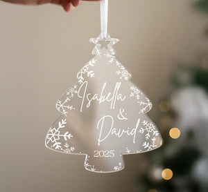 A hand holding a transparent ornament shaped like a Christmas tree with snowflakes and the names "Isabella & David" written on it.