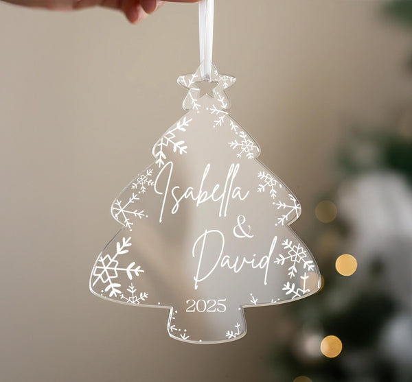 A hand holding a transparent ornament shaped like a Christmas tree with snowflakes and the names &quot;Isabella & David&quot; written on it.