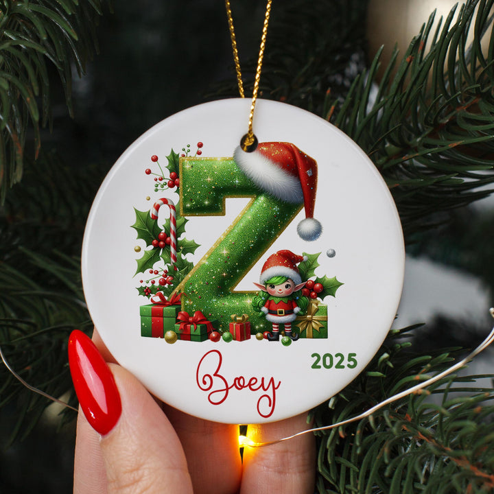 A hand holding a round ornament with a Christmas tree in the background.