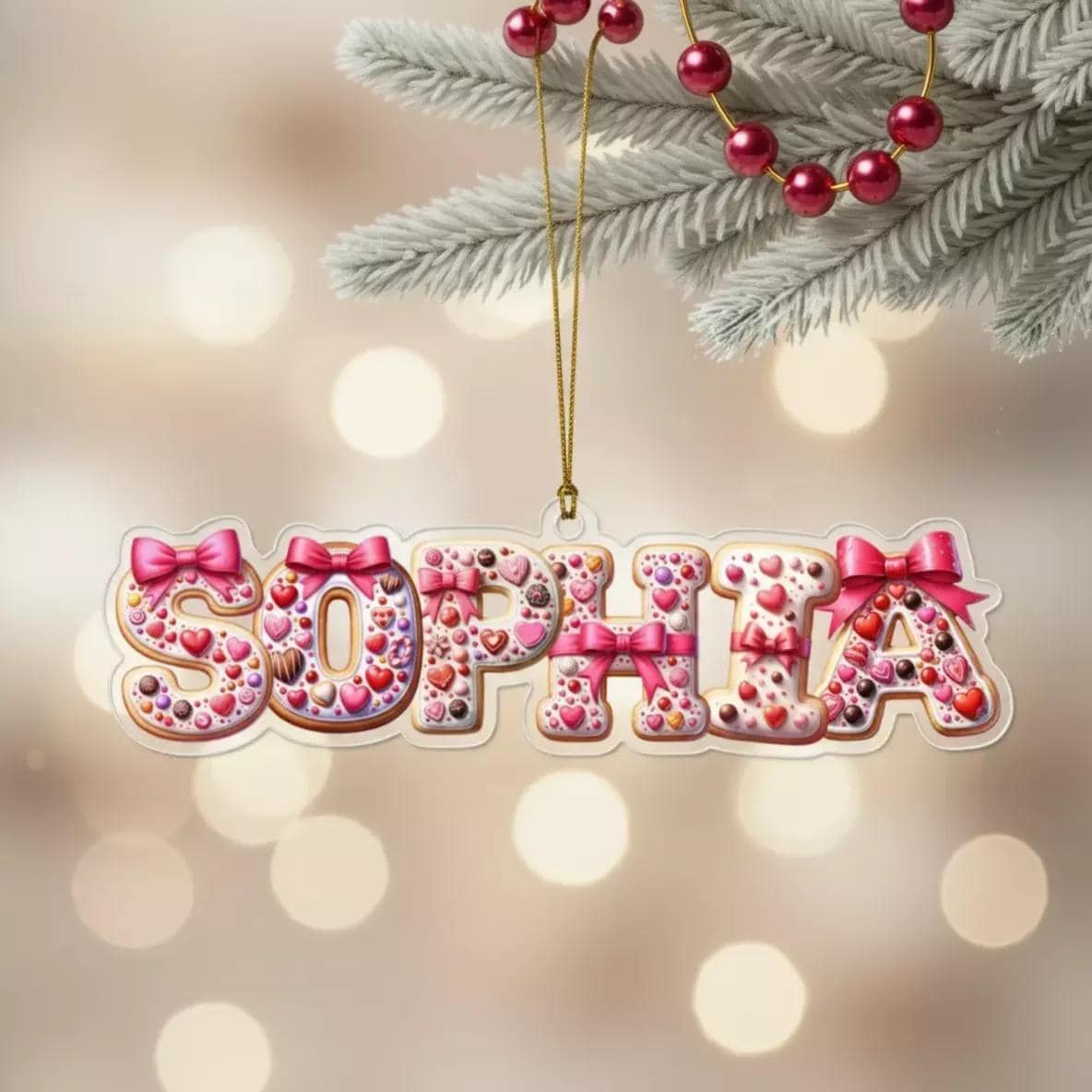 A clear ornament shaped like the name "Sophia" made of cookies and decorated with pink bows and hearts.