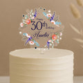 A white cake with a decorative floral topper that says "Happy 30th birthday Amelia".