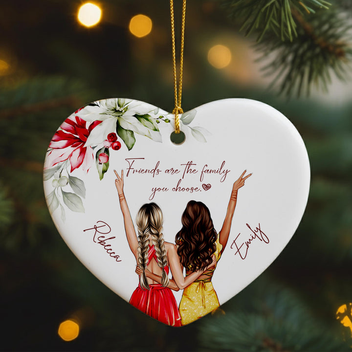 A heart-shaped ornament featuring two women with braided hair, wearing red and yellow dresses, and the text &quot;Friends are the family you choose&quot; written on it.